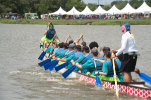 Team with blue shirts in the water rowing their dragon boat