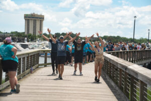 Four people walking down the dock smiling with their hands in the air