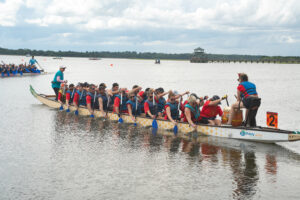 Dragon boat team with red shirts and blue life jackets paddling their boat in the water
