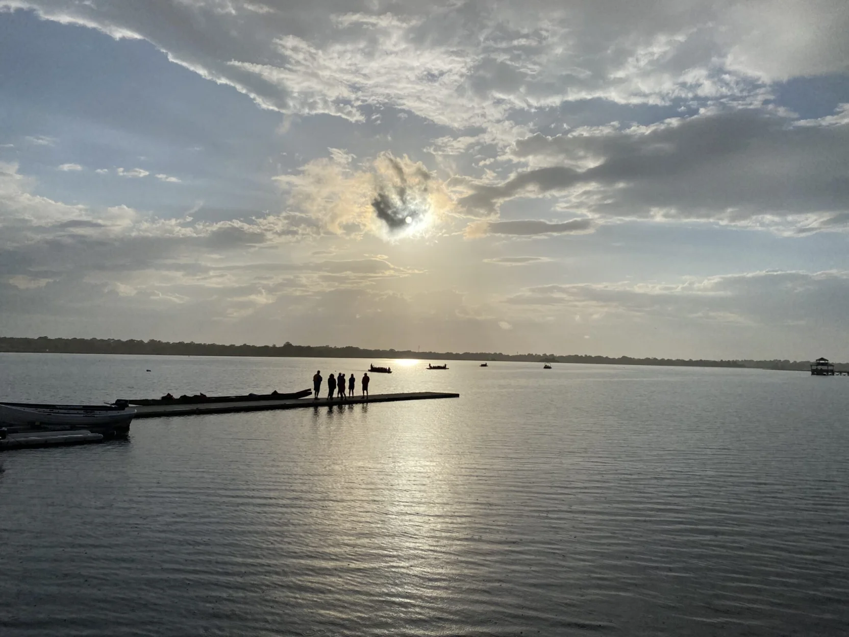 Sun over the water and people standing on the dock admiring the dragon boats